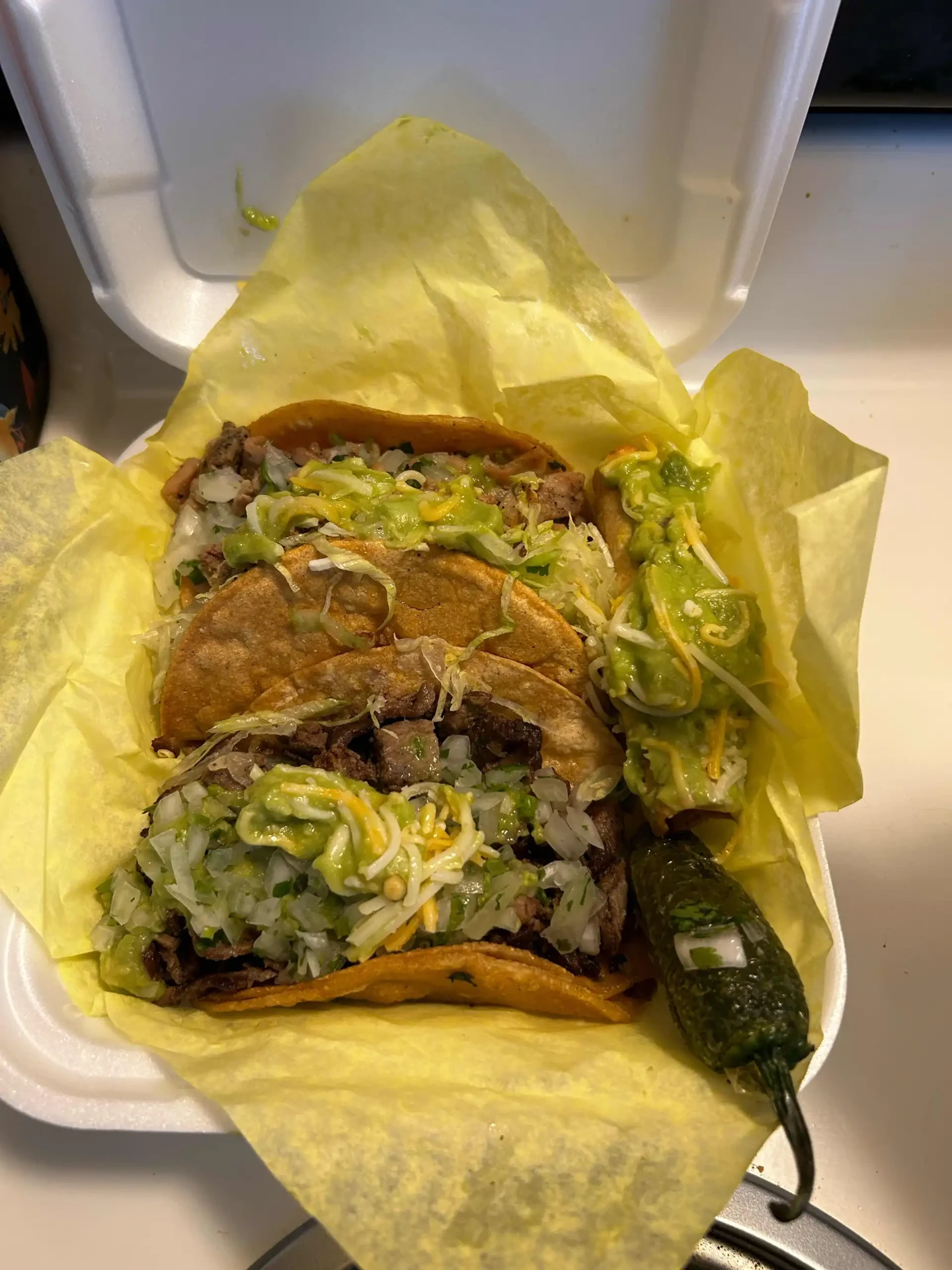 Three tacos and rolled tacos with guacamole in a takeout container